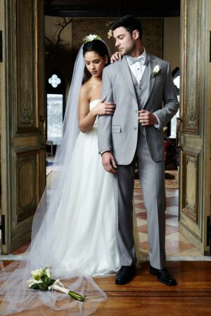 A bride and groom pose together the groom is wearing a well fitted Aspen suit in Heather Grey