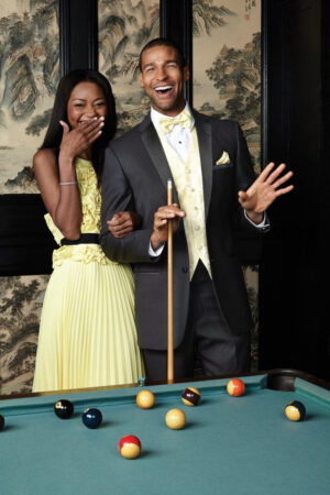 A young man and his date are having a good time at a pool table the man is dressed in the heritage tuxedo