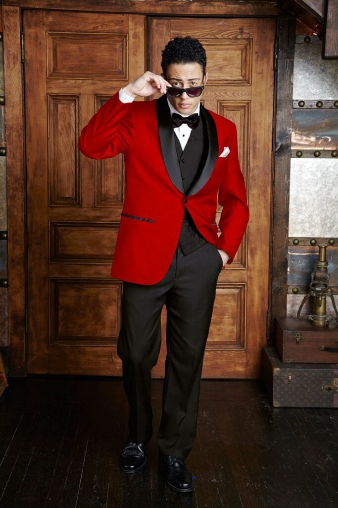 A model poses in a rustic setting, he is wearing a red Bradford Shawl tuxedo rental.