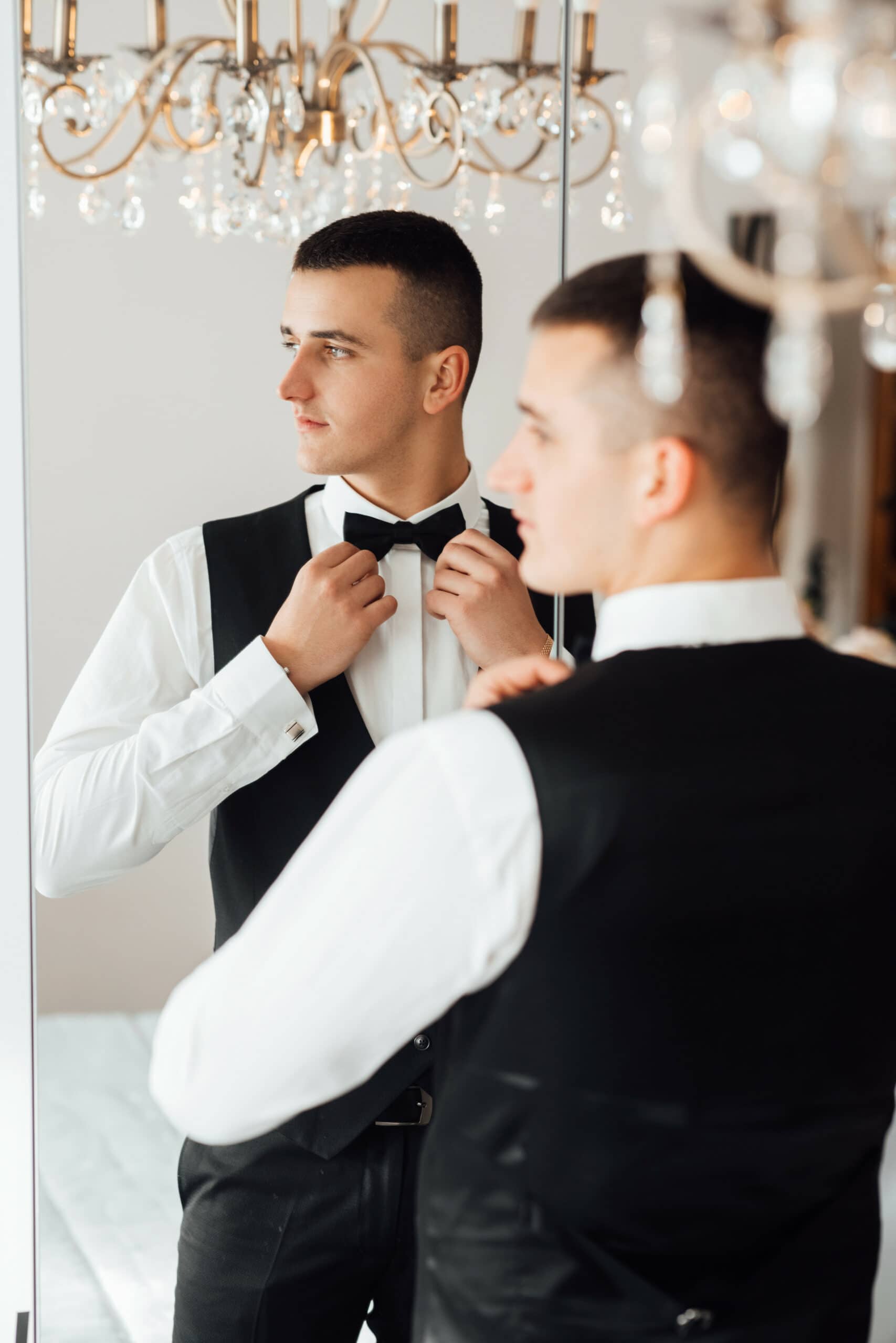 man trying on a tuxedo rental at home in a mirror
