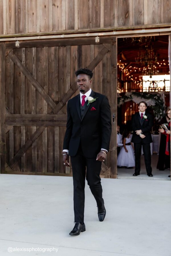 a groomsman wearing a black tuxedo rental walking down wedding aisle
