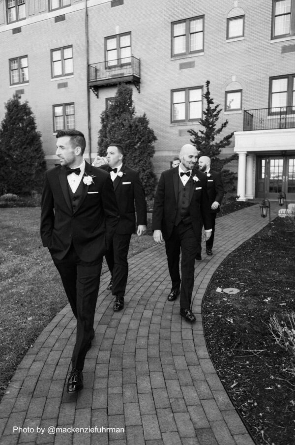 groom and his groomsmen walking on a stone path wearing tuxedos