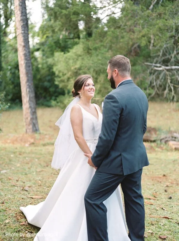 bride and groom holding hands and smiling at each other outside in the grass