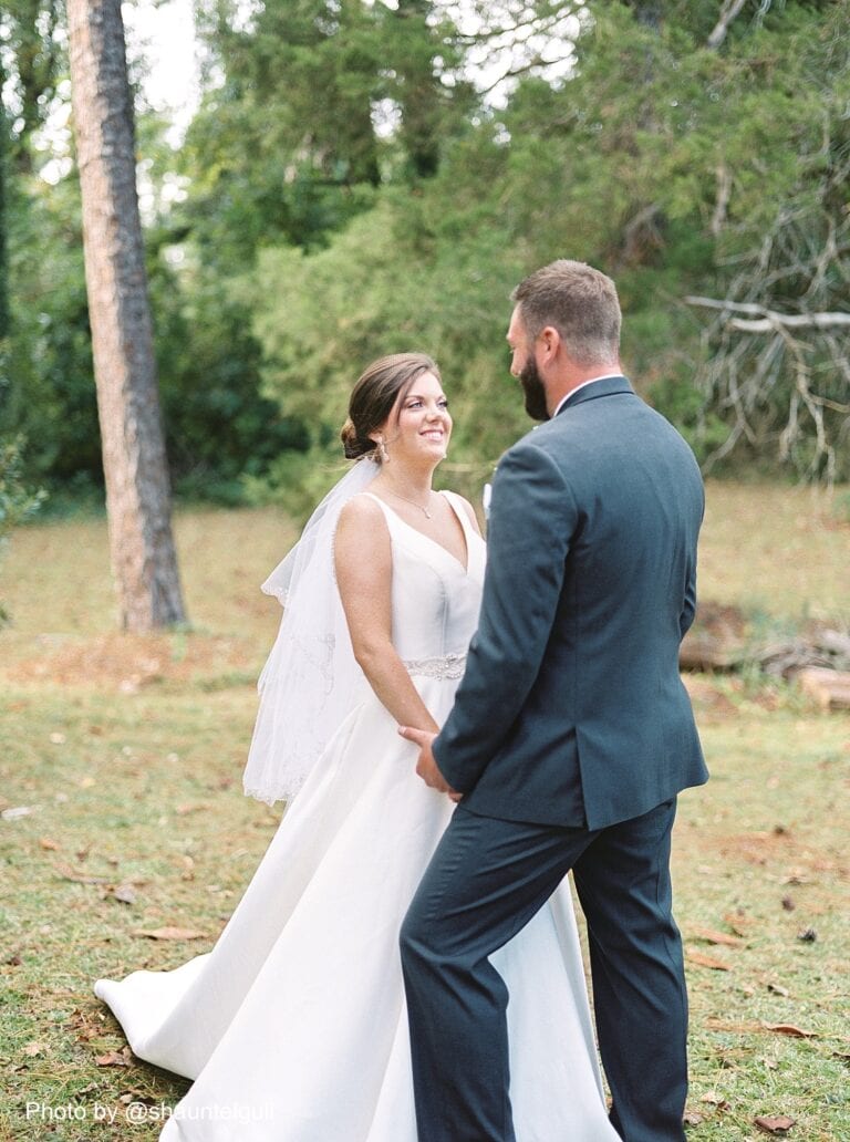 bride and groom holding hands and smiling at each other outside in the grass
