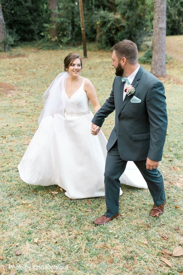a groom wearing a steel grey tuxedo rentals walking in the grass with his bride in her wedding dress