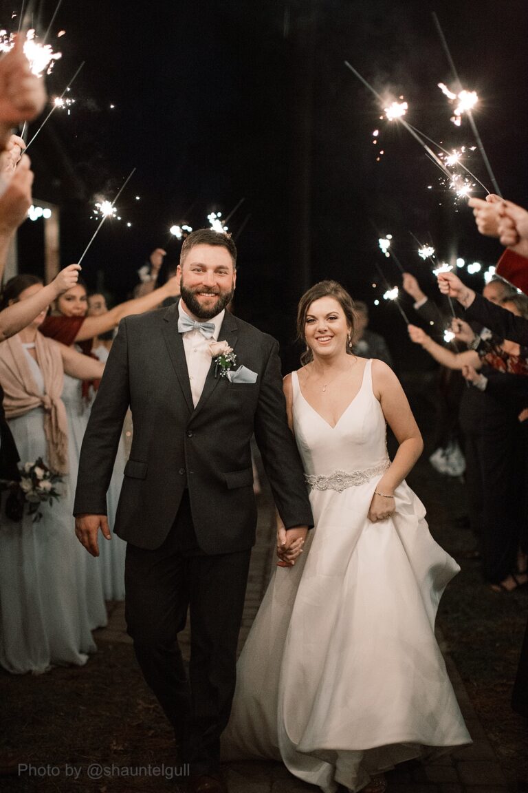 bride and groom walking through a crowd holding sparklers at night time wedding