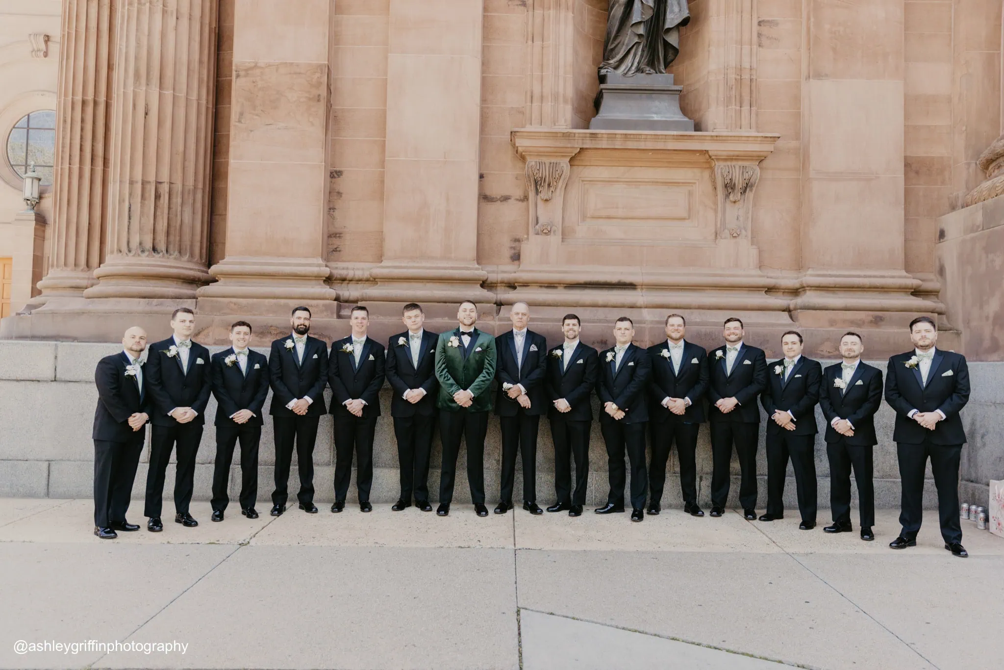 a groom wearing a green tuxedo rental standing outside of a church with his groomsmen