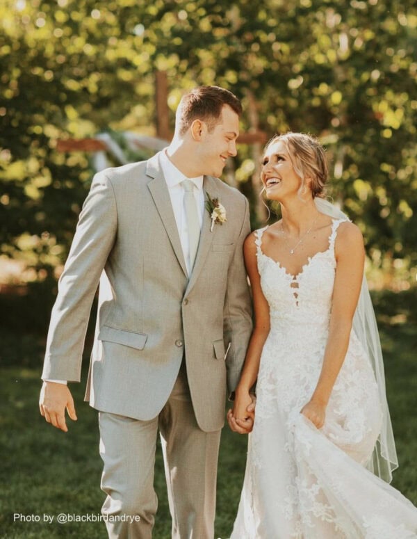 a bride and groom smiling at each other walking outside on a sunny day