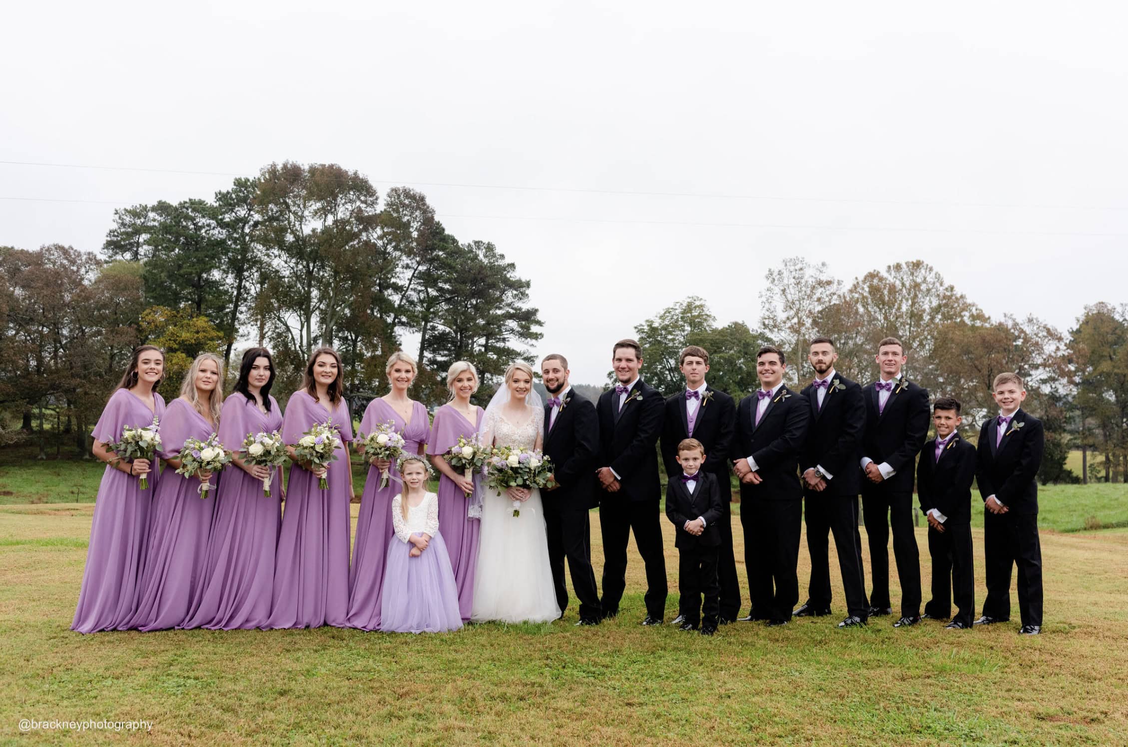 entire wedding party smiling for a wedding photo outside on grass