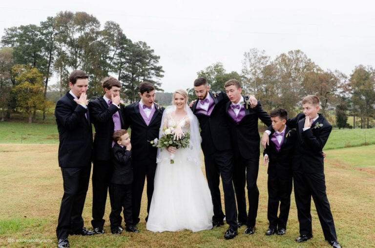 groomsmen wearing black and purple tuxedo rentals standing out bride looking at her wedding ring