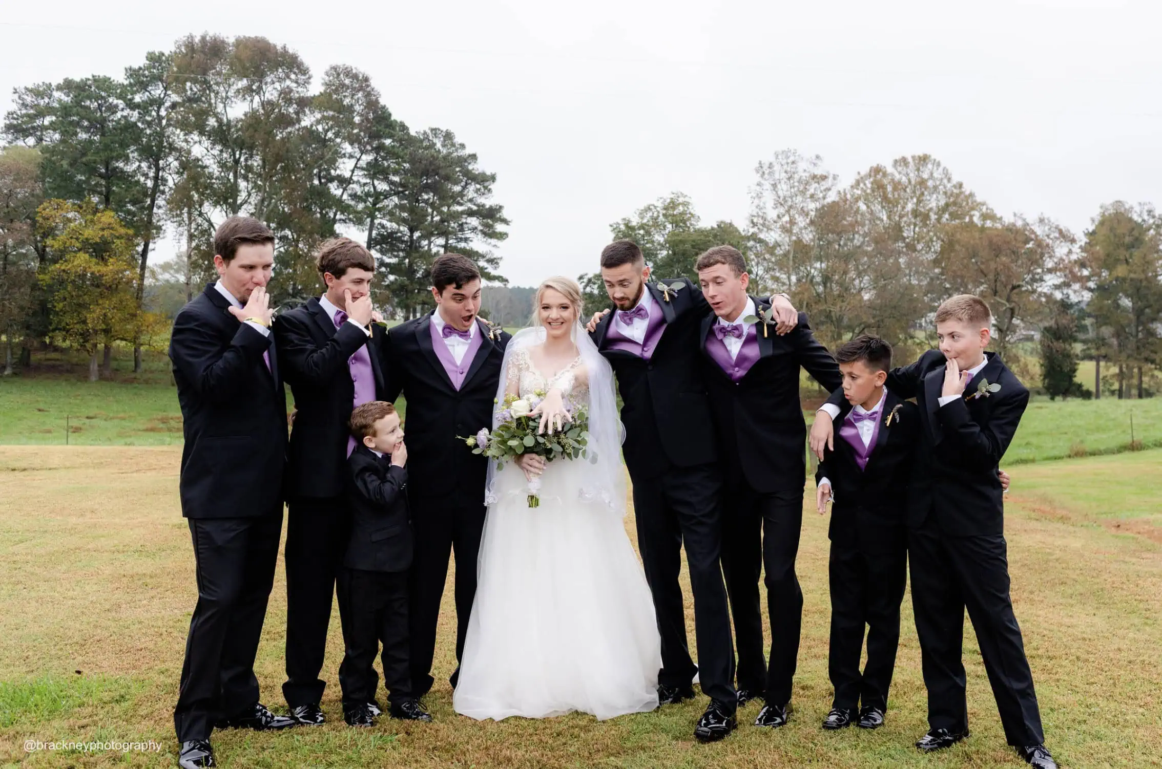 groomsmen wearing black and purple tuxedo rentals standing out bride looking at her wedding ring