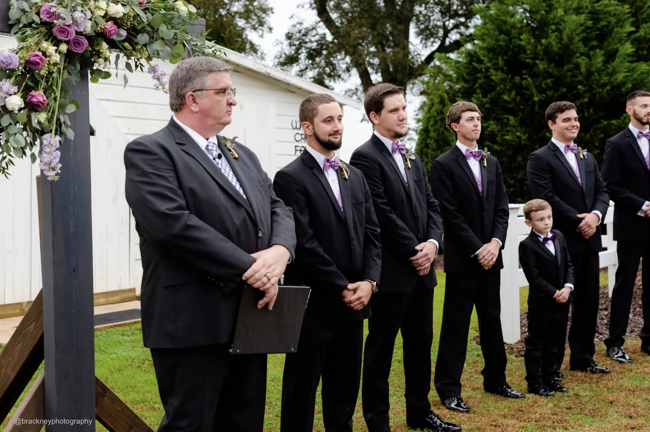 groomsmen and groom wearing black tuxedos standing at the alter waiting for bride to walk down