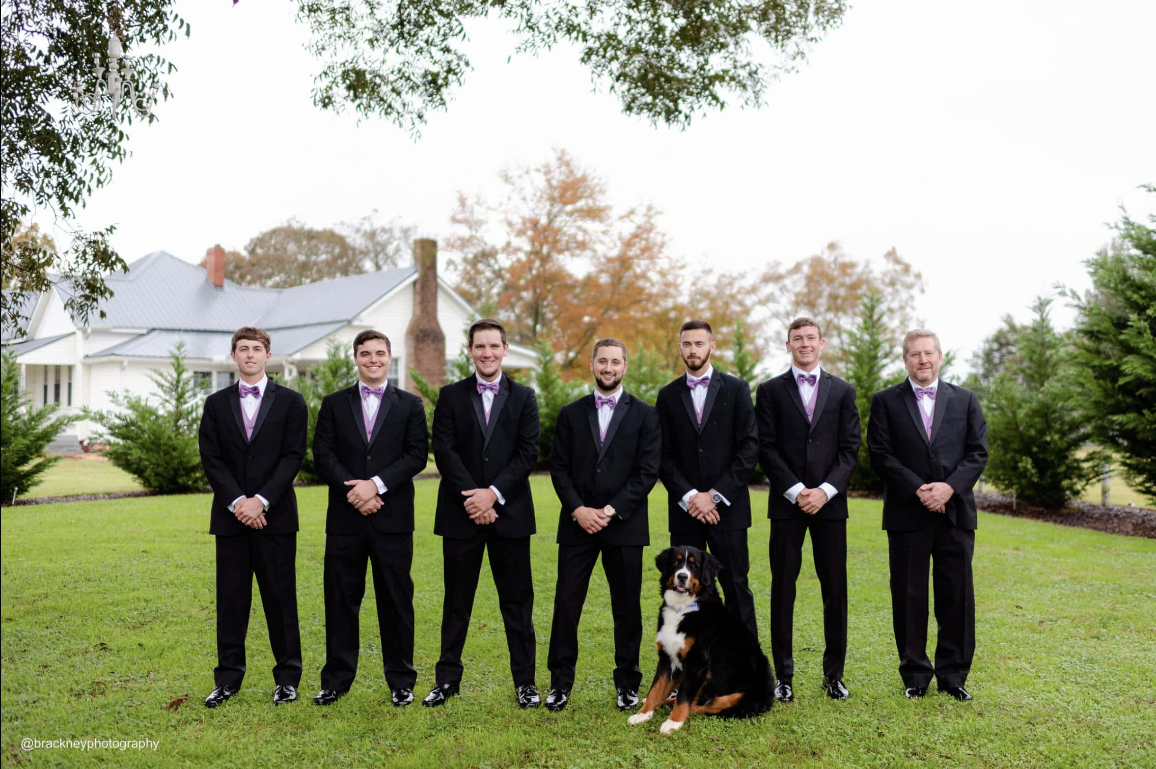 groom and his groomsmen wearing black tuxedo rentals standing outside posing for photo with dog
