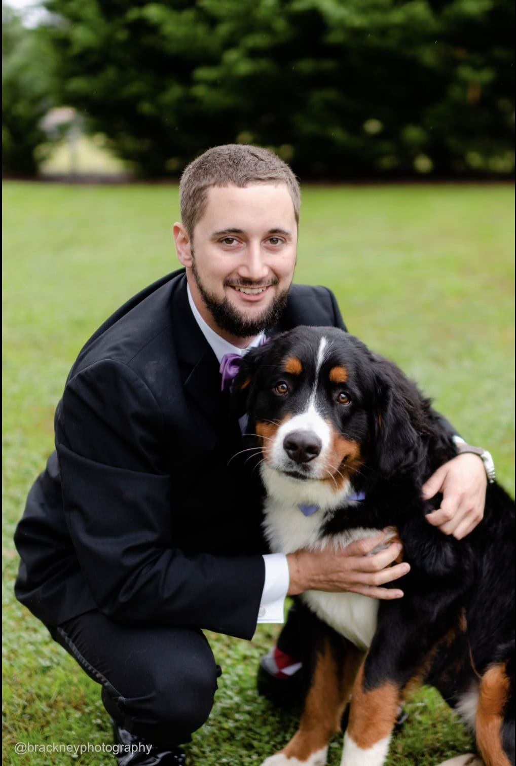 groom wearing a black tuxedo rental posing with his dog
