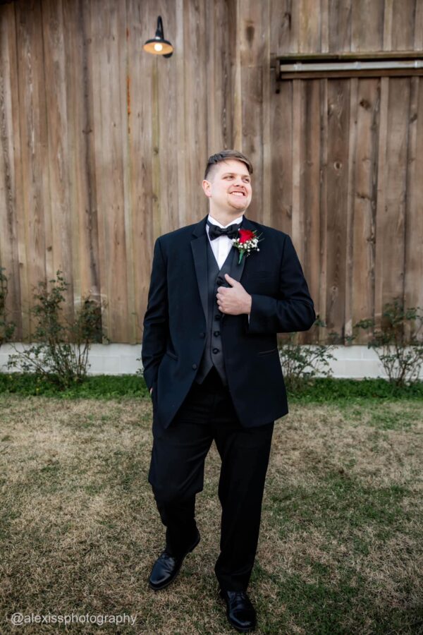 a groom wearing a black tuxedo rental standing outside at wedding