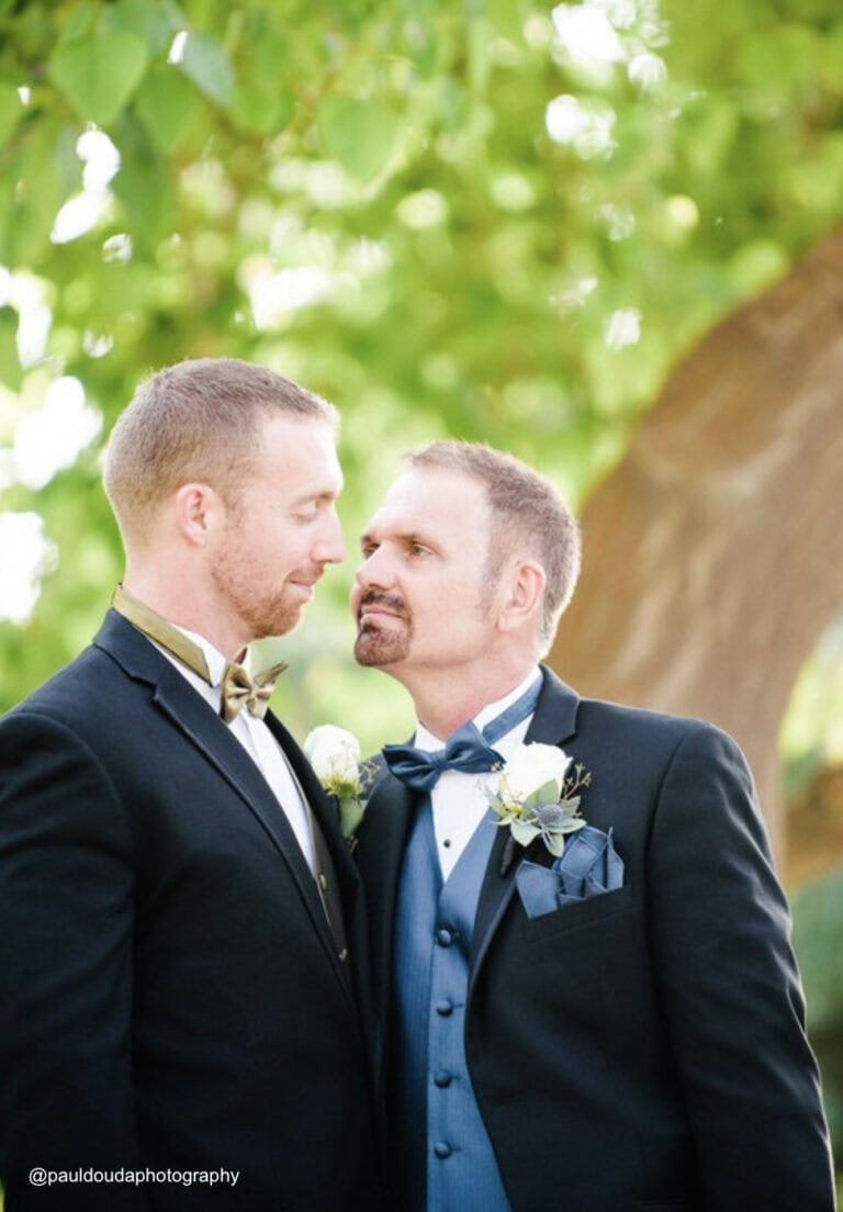two men waring black tuxedo rentals smiling at each other at wedding