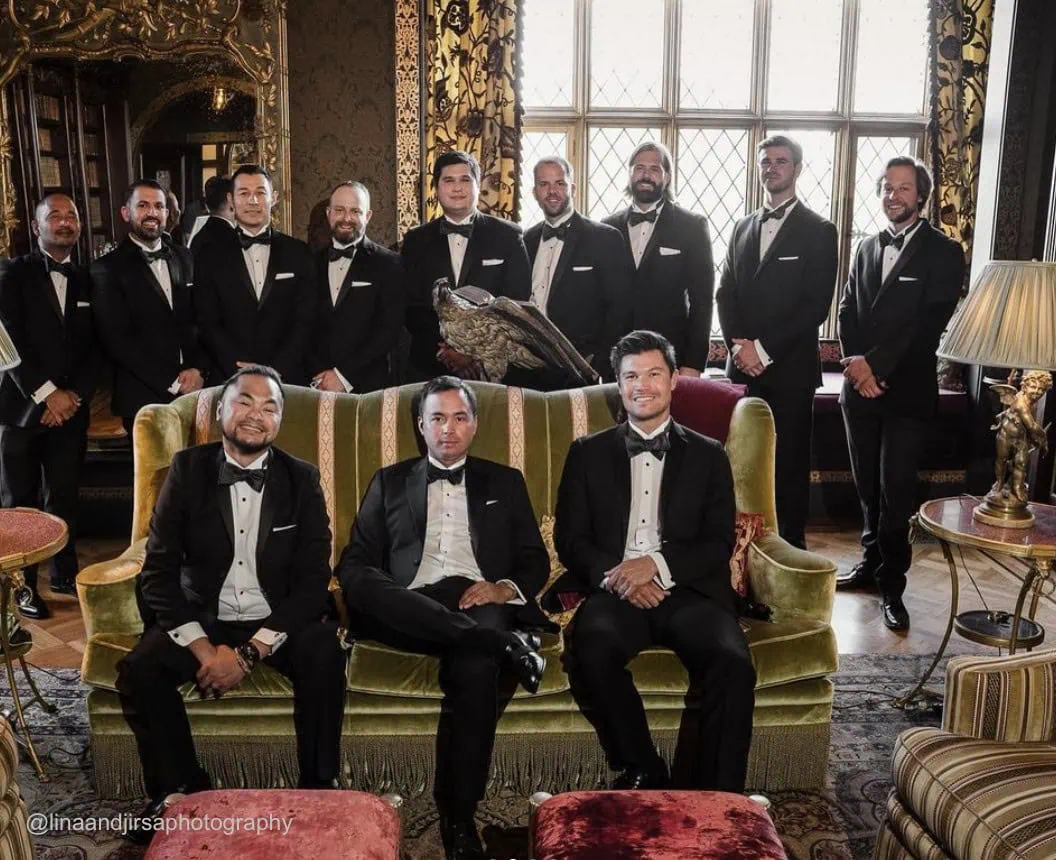 a photo of groomsmen wearing black tuxedo rentals sitting on a couch in a victorian style home