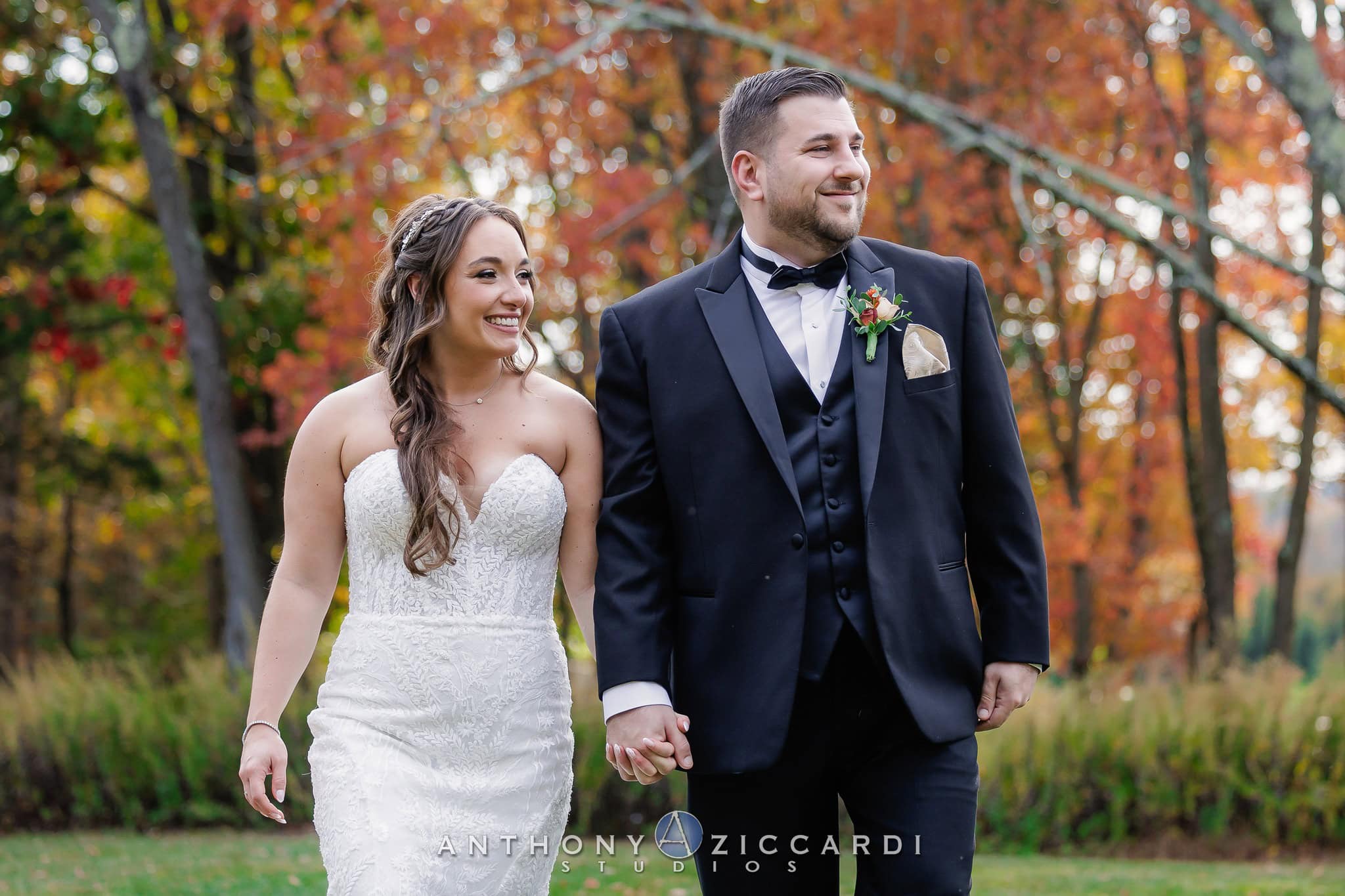 groom wearing a balck tuxedo rental walking with bride at outdoor fall wedding