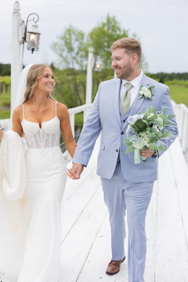 4042231F-5424-4AA6-B575-E0F6C9C3D6BA | National Tuxedo Rentals bride and groom walking on white bridge