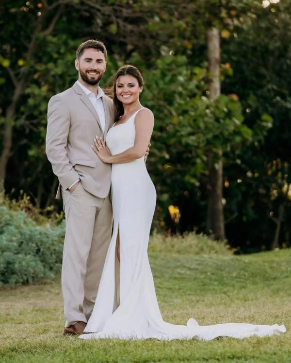 groom wearing tan suit standing with bride outdoors