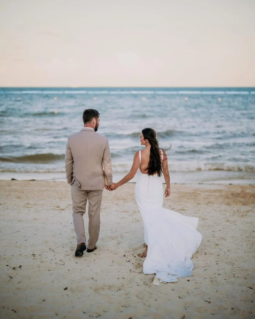 groom wearing tan suit rental walking on beach with bride