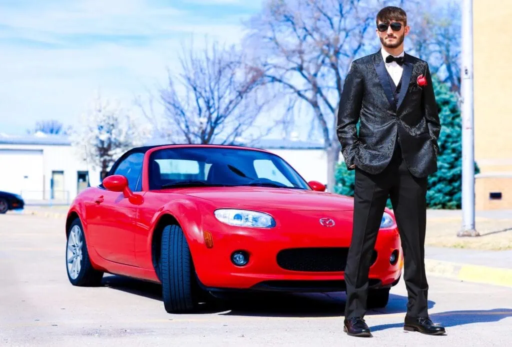 young man standing in front of red car wearing a prom tuxedo rental