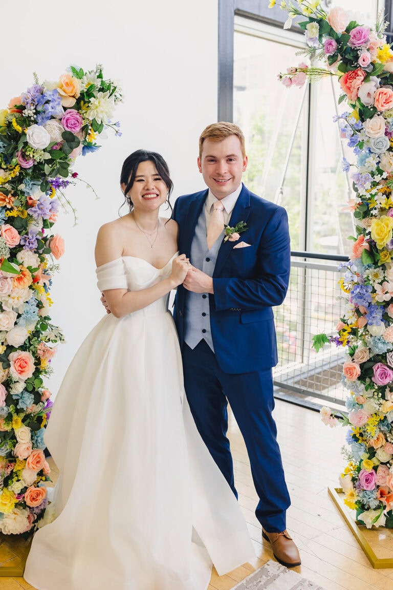 bride and groom standing under flower arch