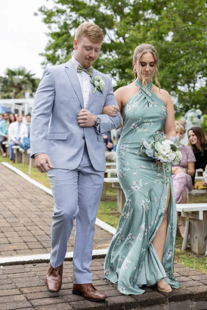 groomsman walking down aisle with bride wearing blue suit rental