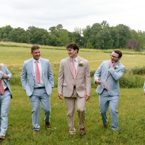 groom and groomsmen in blue suits walking in field