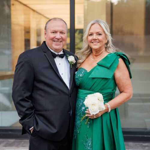 Man wearing black tuxedo rental with date in green dress