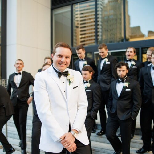groom wearing white tuxedo with groomsmen in black tuxedos