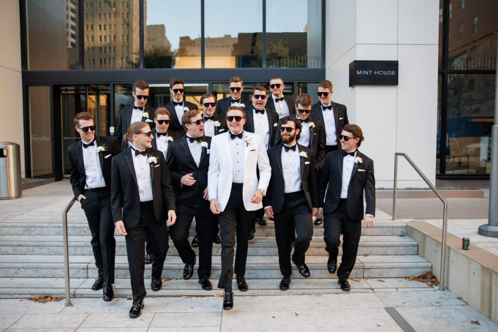 grooms in white tuxedo rental walking down stairs with groomsmen