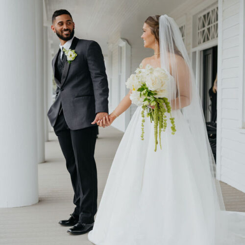 bride and groom standing on white porch holding hands