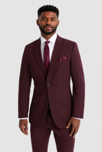 Man wearing a burgundy suit with white shirt and matching tie, standing against a light backdrop.