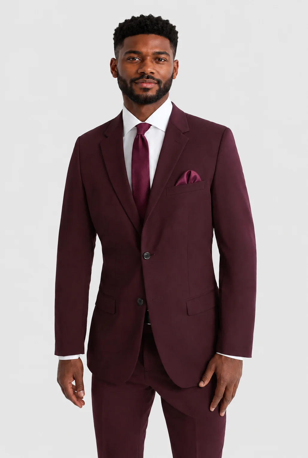 Man wearing a burgundy suit with white shirt and matching tie, standing against a light backdrop.