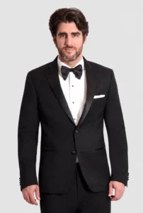 Man wearing a black tuxedo with bow tie and white pocket square, posing against a light background.