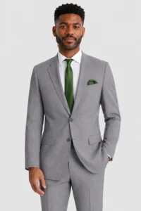 Man in a light gray suit with a green tie, standing against a light background.