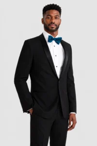 Man in a black tuxedo with a white shirt and blue bow tie, posing against a light background.