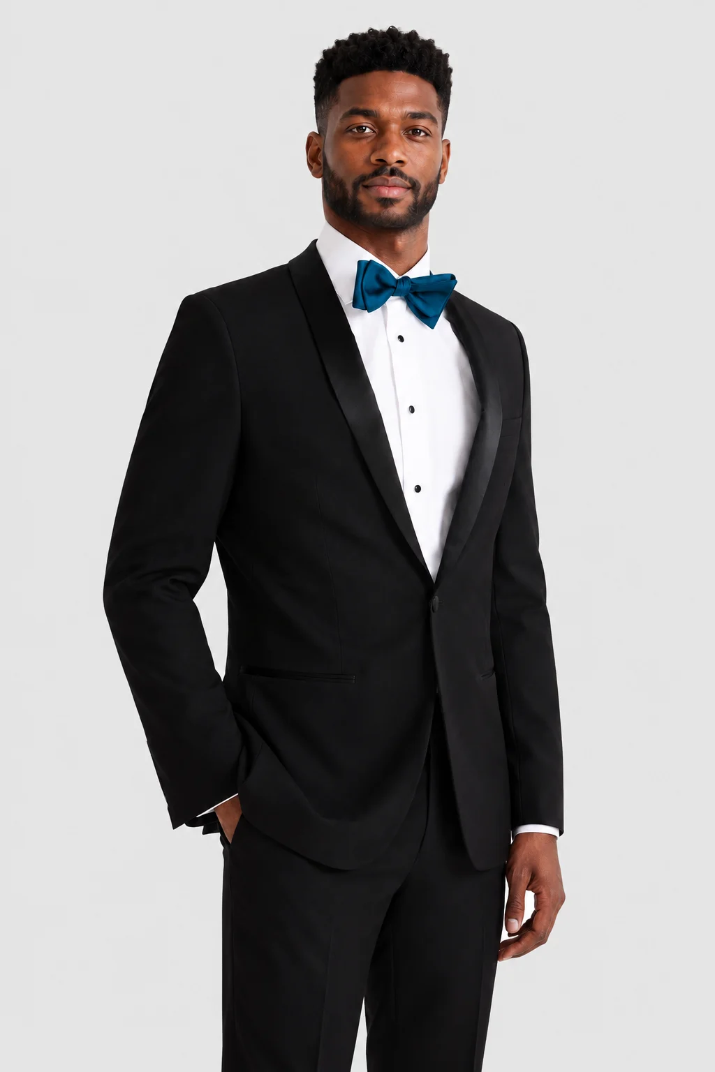 Man in a black tuxedo with a white shirt and blue bow tie, posing against a light background.