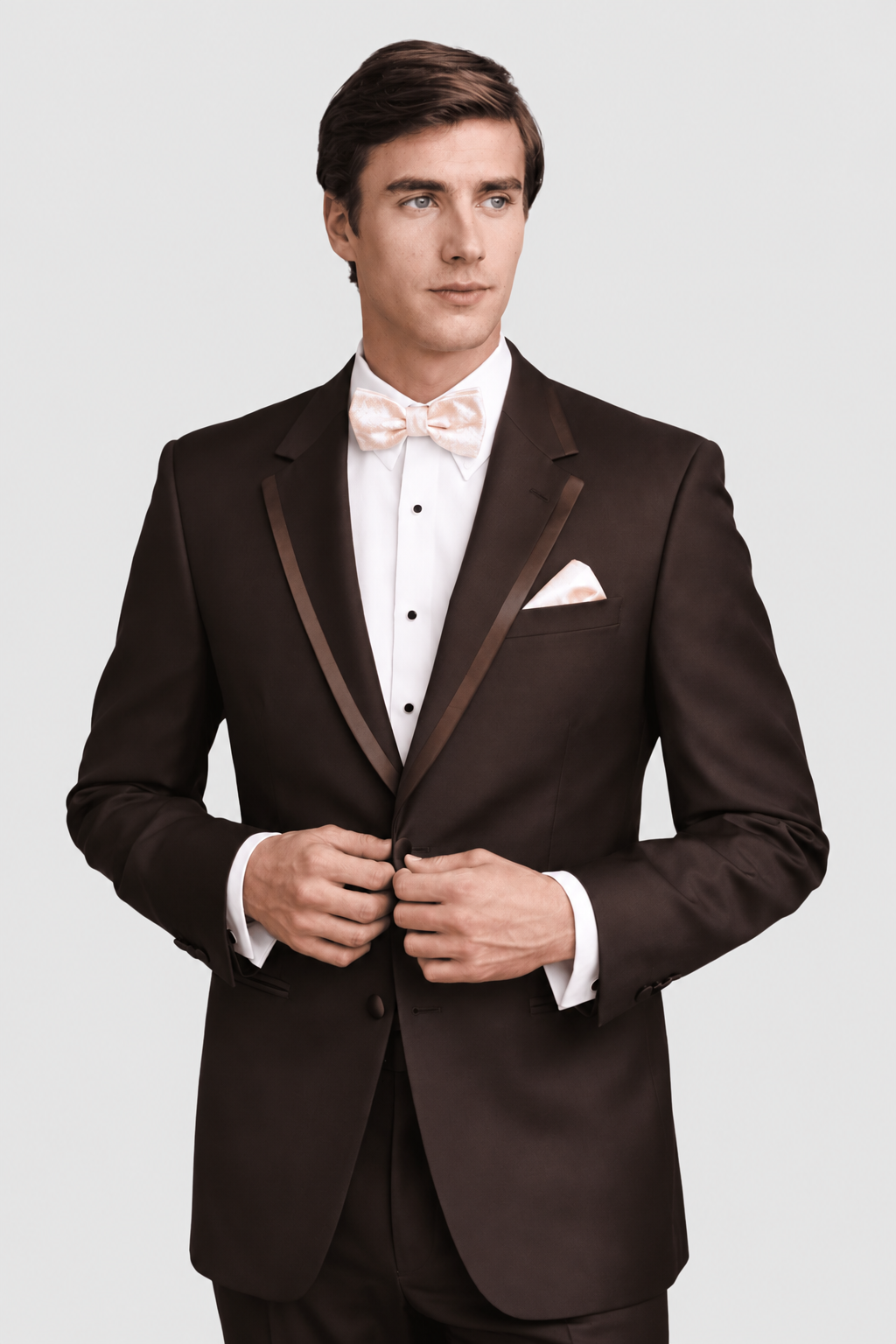 Man in a brown tuxedo with satin lapels, white shirt, pink bow tie, adjusting his jacket.